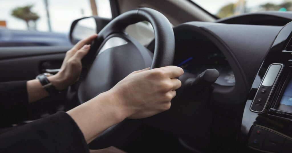 A person is driving a car with their hand on the steering wheel